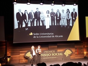 Eva Valero, "directora de Sedes", recogiendo el premio con la foto de los directores de las Sedes de la UA de fondo